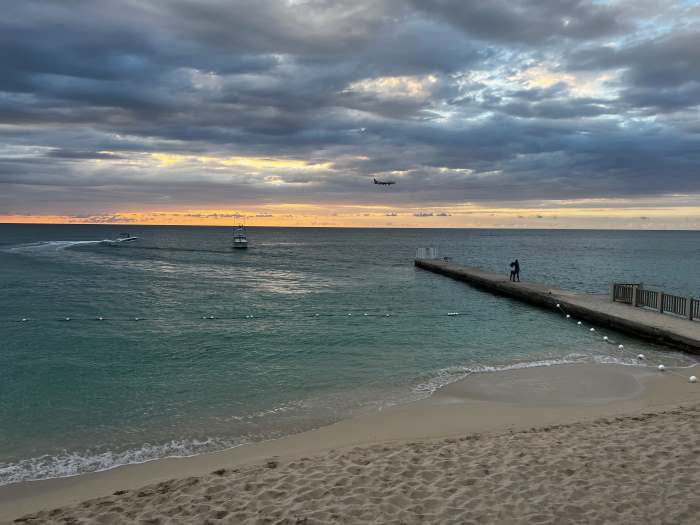 A golden sandy beach and crystal clear water right after sunset with the golden glow over the water in the distance