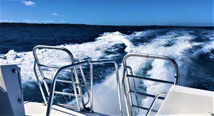 Beautiful view of the whitewater behind a boat cruising on dark blue water under a bright blue sky