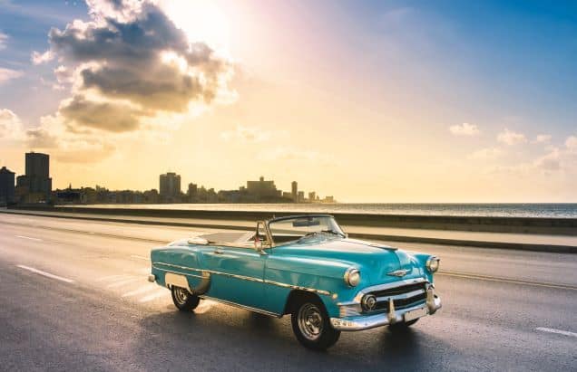 Day trip to Cuba from Miami: classic American car driving along the Malecon boardwalk in Havana in sunny weather before sunset
