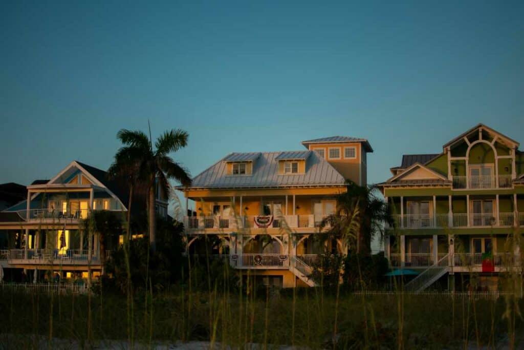 Sunset ambiance with a deep blue sky behind a row of charming wooden houses that glow in the sunset, on a summer evening with green grass and palm trees