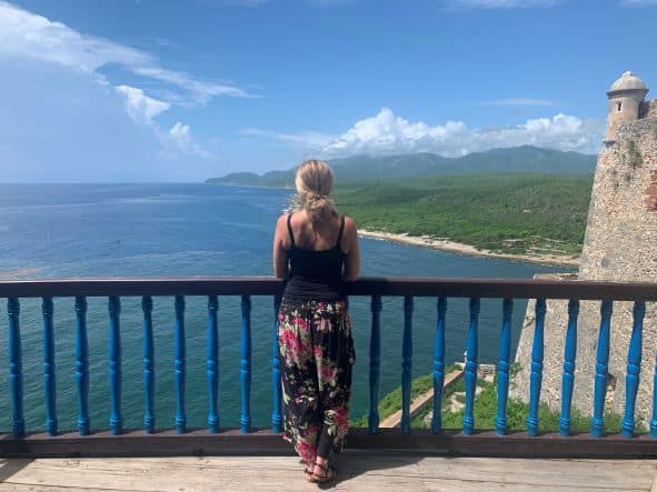 Woman standing on a balcony high above the ocean on a fortress, looking at the view and the horizon on a sunny day with blue skies