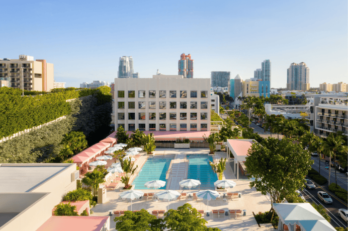 Overview photo off a stunning hotel pool and lounge area with the blue water, white and blue parasols, and delicate grounds to relax and recuperate under a blue sky and sunny summer day