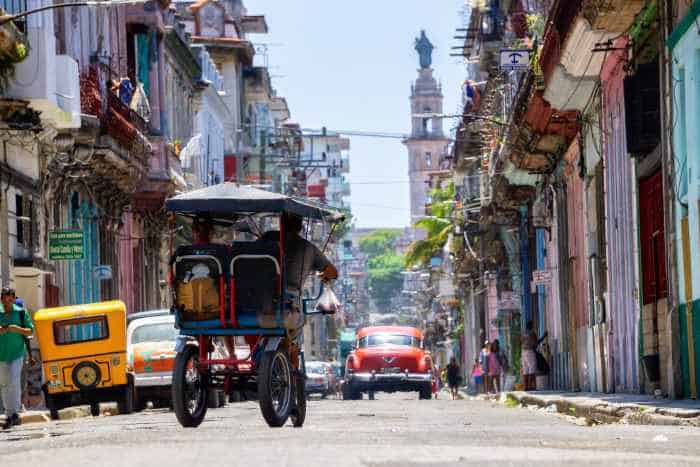 Cuba travel hacks. How to travel from Canada to Cuba. Bicycle taxi in the streets of central havana narrow streets surrounded by colonial architecture buildings.