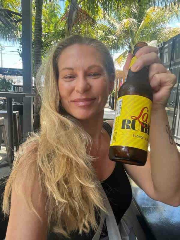 Me (a blond) smiling at the camera with a bottle of Rubia beer during a food and art tour in Wynwood Miami