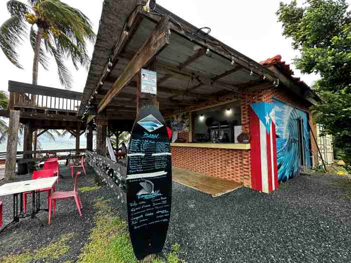 The Lighthouse Cafe in Rincon, Puerto Rico where the menu is written on a surfe board, and the cafe is an open air space under ceiling surrounded by palm trees with stuning views of the ocean