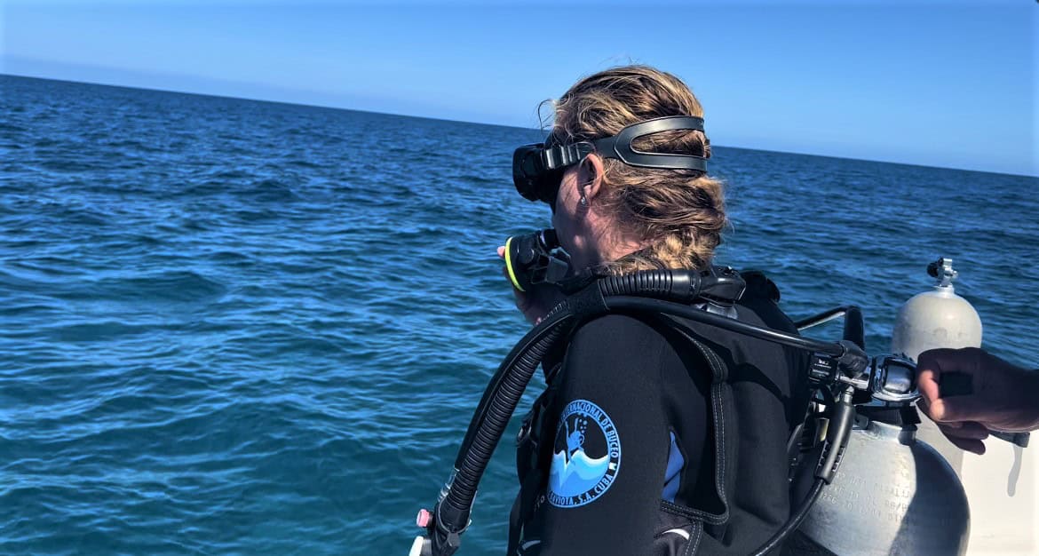 Lady wearing scuba diving gear about to exit from a boat into the dark blue sea on a sunny day