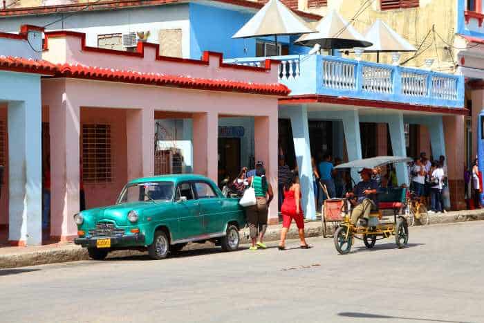 How to travel to Cuba: travel tips from an expert. Photo of classic colonial architecture houses and a bright green classic American car.