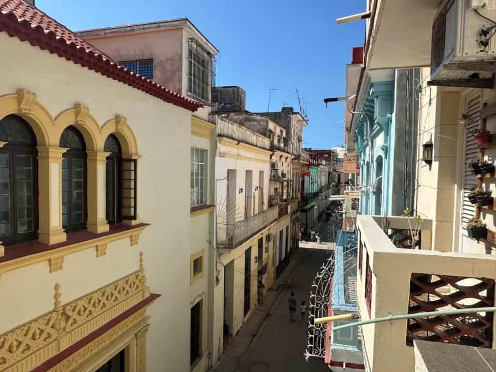 A narrow street with tall exquisitely decorated colonial buildings in paster colors with intricate ornaments and small balconies under a blue summer sky in Havana, Cuba. 
