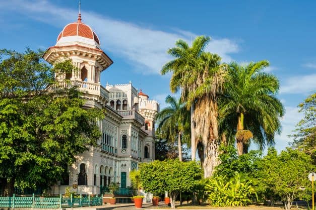 A classic colonial palace surrounded by green trees and palm trees on a bright sunny day