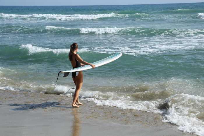 A woman heading into the waves with a surfing board on a sunny day