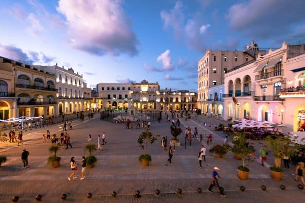 a large plaza at sunset with warm light from the golden sky and lots of people strolling in the plaza