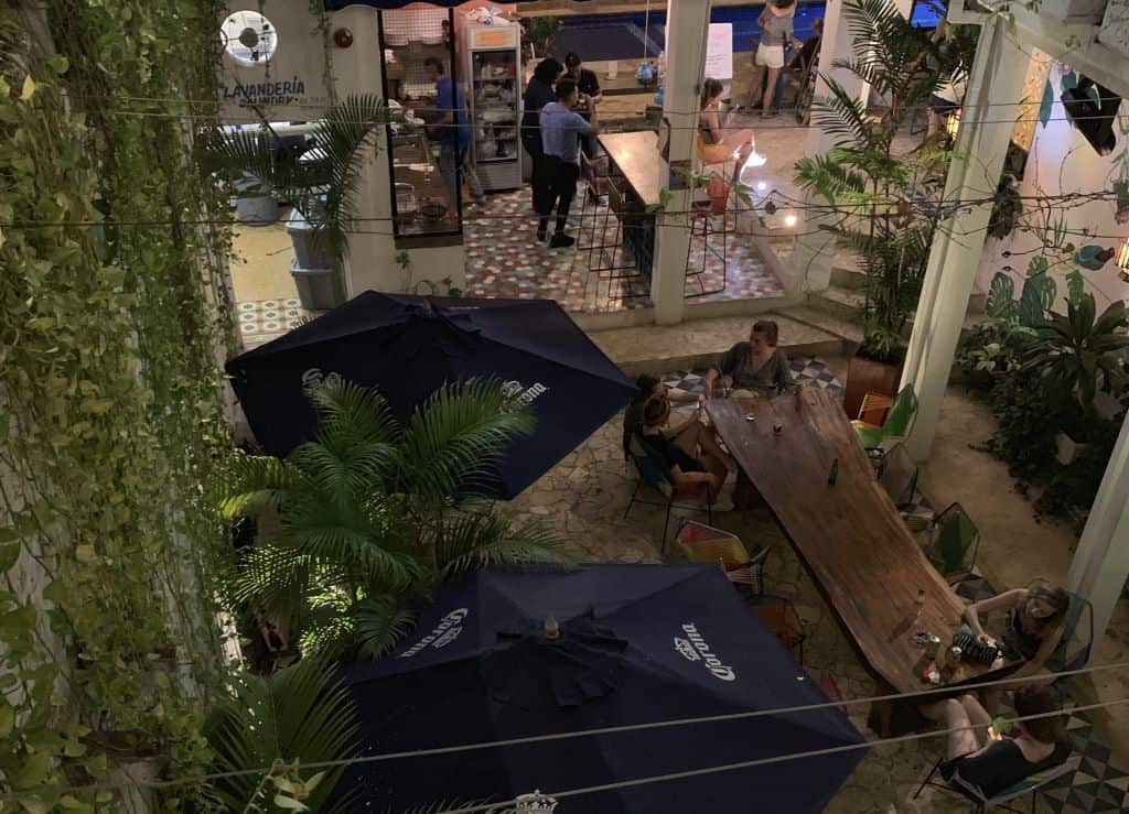 A beautiful courtyard at night with tables and a bar and green plants, and lots of people enjoying themselves