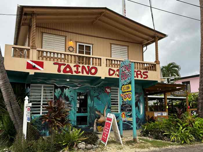 Taino Divers dive shop, in a yellow wooden house with green water-colored signs and red name sign sitting next to the beach in Rincon will take you scuba diving from Rincon