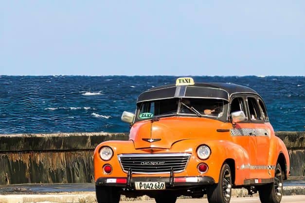 Is there Uber in Cuba? A bright yellow classic American car taxi driving along the Havana Malecon