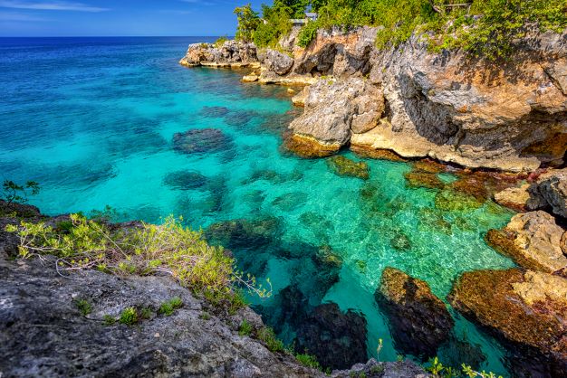 Stunning crystal clear blue waters below rocky cliffs on a sunny summer day