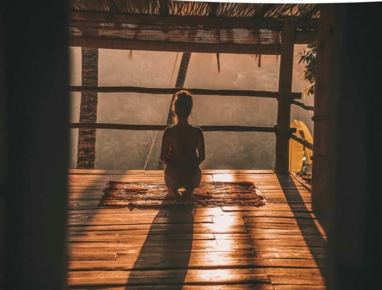 Why is travel important: woman sitting on a yoga mat in Bali during sunset with infinite views.