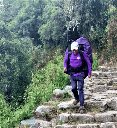 A sherpa carrying a huge backpack on the rocky trail of the Inca Trail