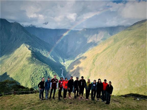 A group of hikers on a view point along the inca trail high above a green valley whre a rainbow hangs across the valley