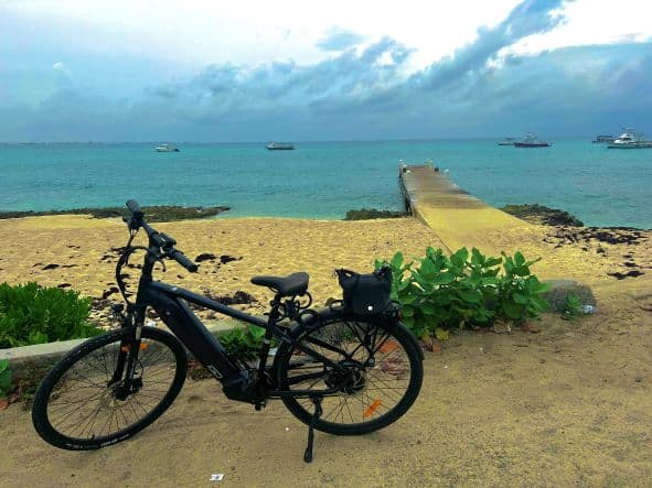 Renting an e-bike and exploring Seven Mile Beach Grand Cayman. This is my bike in front of the beach and a pier, during a break. On the blue waters in the background are several boats. 