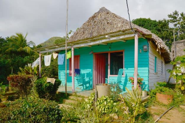 A small charming wooden house painted in light greenish blue with pink window cills in Vinales Valley