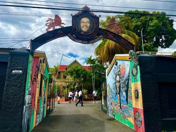 The gate to Bob Marley museum in Kingston Town Jamaica, full of colorful murals, and you can see Bob Marleys house in the background