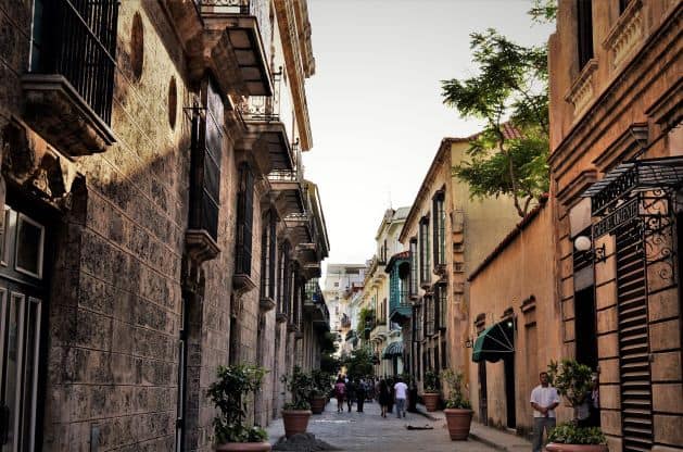 Narrow street in Old Havana, in the middle of old colonial style houses with elaborate details, little balconies, and decorative greenery. 