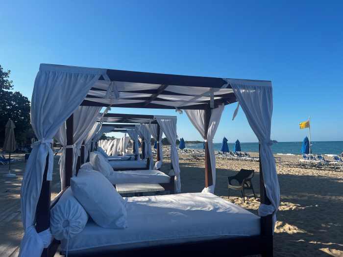 White sandy beach in Puerto Plata, with large double sun beds with curtain ceilings and curtains on all sides to shade you from the sun only meters from the warm water under the blue sky