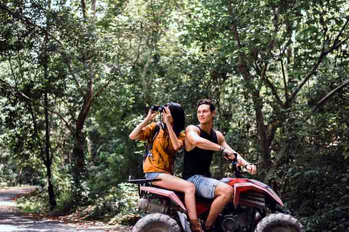 A couple on an ATV tour in green lush forest, smiling and taking photos