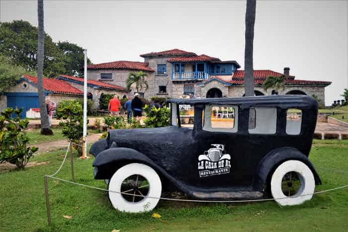 Al Capones old house in Varadero, a huge mansion of grey rock with a red roof and blue details, where he threw lavish parties in the first half of the last century. In front is also a black veteran car with the inscription "La casa de Al", or Als house. 