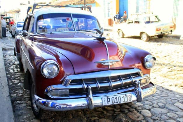 A deep red shiny classic American car on the cobblestoned streets of Trinidad Cuba on a sunny summer day. 