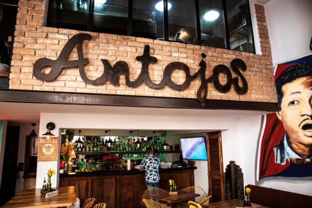 Paladar Antojos in Havana, the netrance with a large sign, the brown wooden bar inside with a person ordering at the counter. 