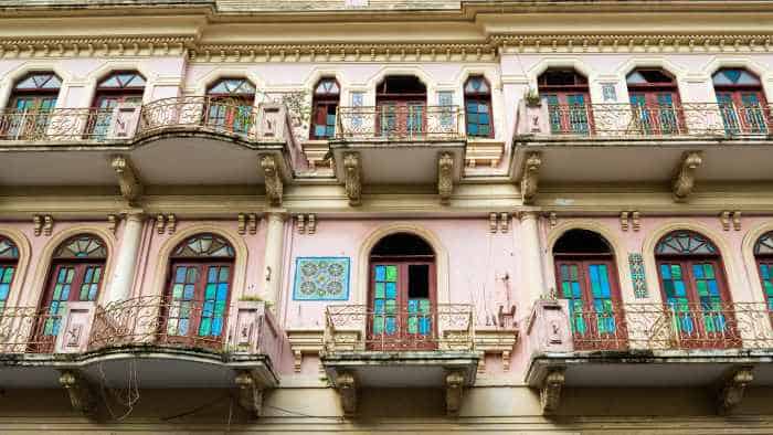 Pale pink building in classic colonial architecture in Santiago, DR, with beautiful balconies, arched windows with colored glass and ornate details on the facade. 
