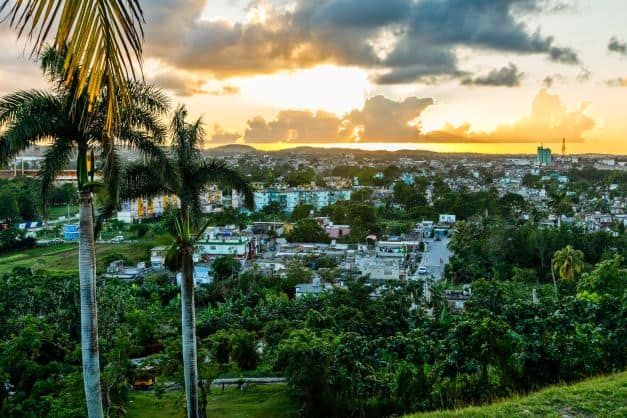 The amazing view from La Loma hill in Santa Clara in Cuba. Below the hill is the town, with lots of trees and grenery, and in the distance you see the golden sunset setting below the horizon. 