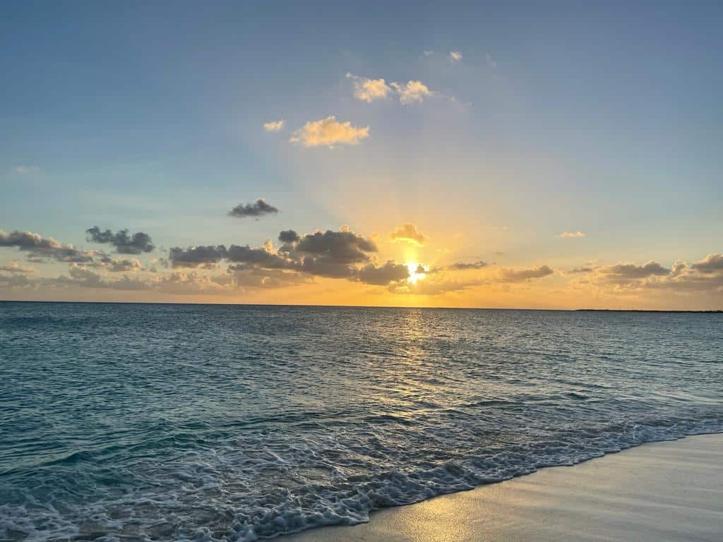 Stunning sunset from a Barbuda Beach, the sky is pale blue, the sun with golden rays in the horizon, and the sea is deep blue right out from the silvery sands