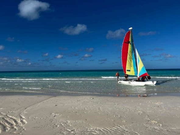 A small white catamaran in the surf in Varadero, with a colorful sail in red, yellow and blue. 