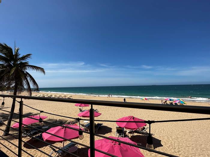 From a beach bar in San Juan, the view of pink parasols on the golden sandy beach, the beutiful blue ocean under the deep blue sky on a bright sunny day. 