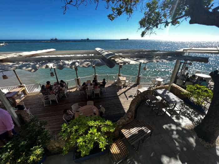 A terraced restaurant by the sea in Santo Domingo, with amazing views from the outdoor seating on wooden floors under a white shading ceiling. 