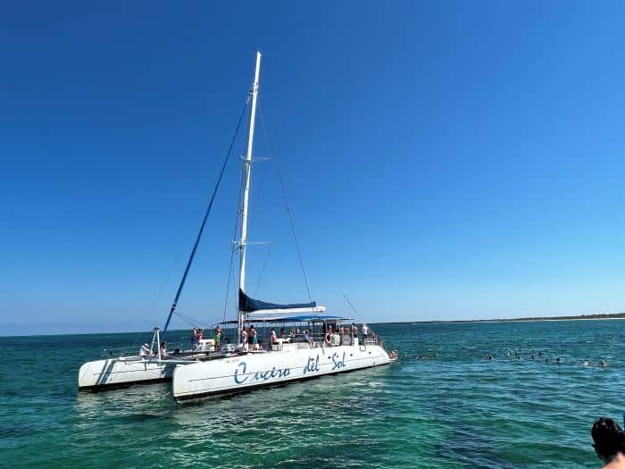 Catamaran tour in Varadero, a white beautiful catamaran on the bluish green water and a group of snorkelers swimming around the boat. 