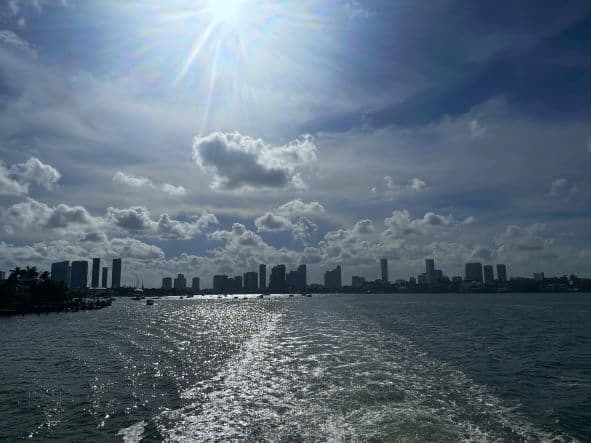 Miami Skyline in the distance from the middle of the Biscayne Bay on a boat trip, the skyline is small and the sea dark blue under hazy air and sunny sky. 