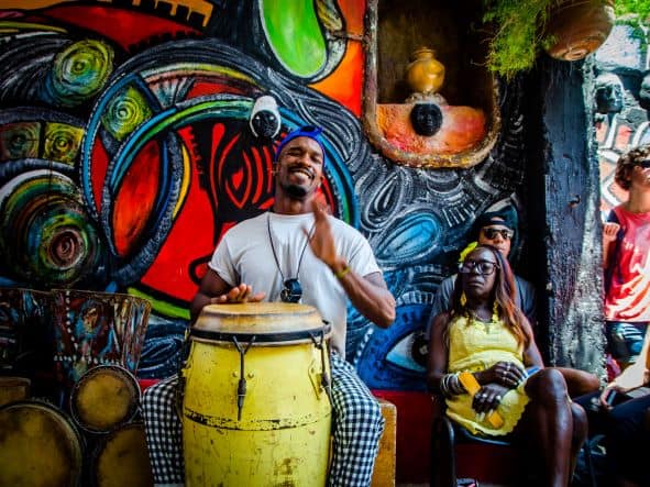 Smiling drummer with a large yellow drum in Callejon de Hamel in Cuba, with seated spectators along the colorful murals in this small but cultural important alley. 
