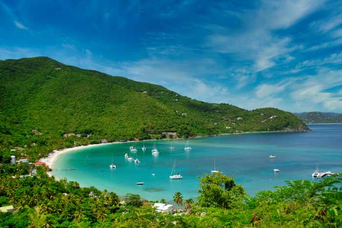 The blue waters with lots of sail boats in Cane Garden Bay on Tortola, below lush green hills on a sunny summer day with blue skies
