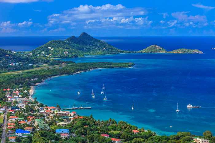 The unreal blue waters in Carriacou, Grenada, with white boats on the water close to the shores with colorful rooftops and green hills