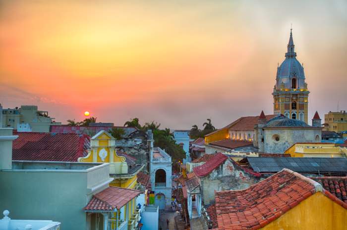 Cartagena de Indias cityscape at sunset, with a mixture of different roods, colored building, a church tower in the distance, and the glowing sunset in the background