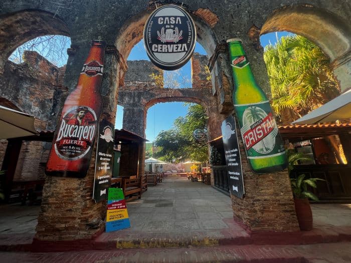 The entrance to Casa de Cerveza in Trinidad, flanked with big posters of bear bottles on stone columns, and inside there are outdoors seating and a charming atmosphere with grey stone floors and wooden furniture. 