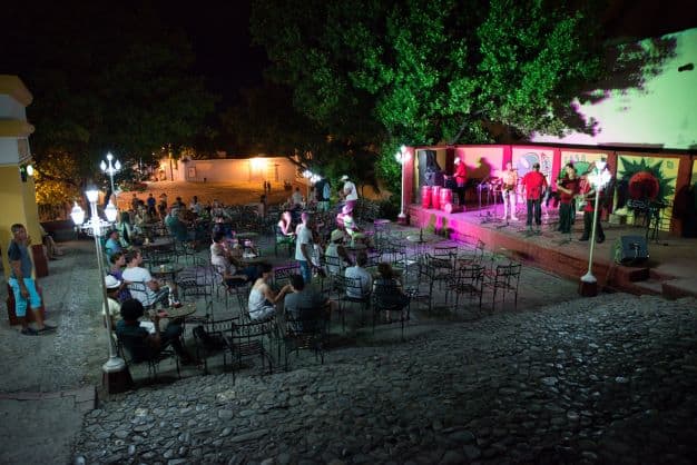 Casa de la Musica in Trinidad at night, in the middle of a cobblestoned plaza. People seated on outdoor seating, and a band playing salsa music from the stage. 