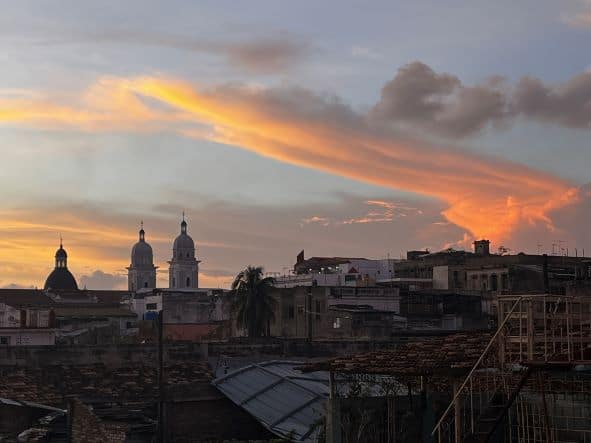 The towers of the cathedral of Santiago de Cuba visible in the distance behind a sea of rooftops around sunset with glowing colours on the clouds in the sky