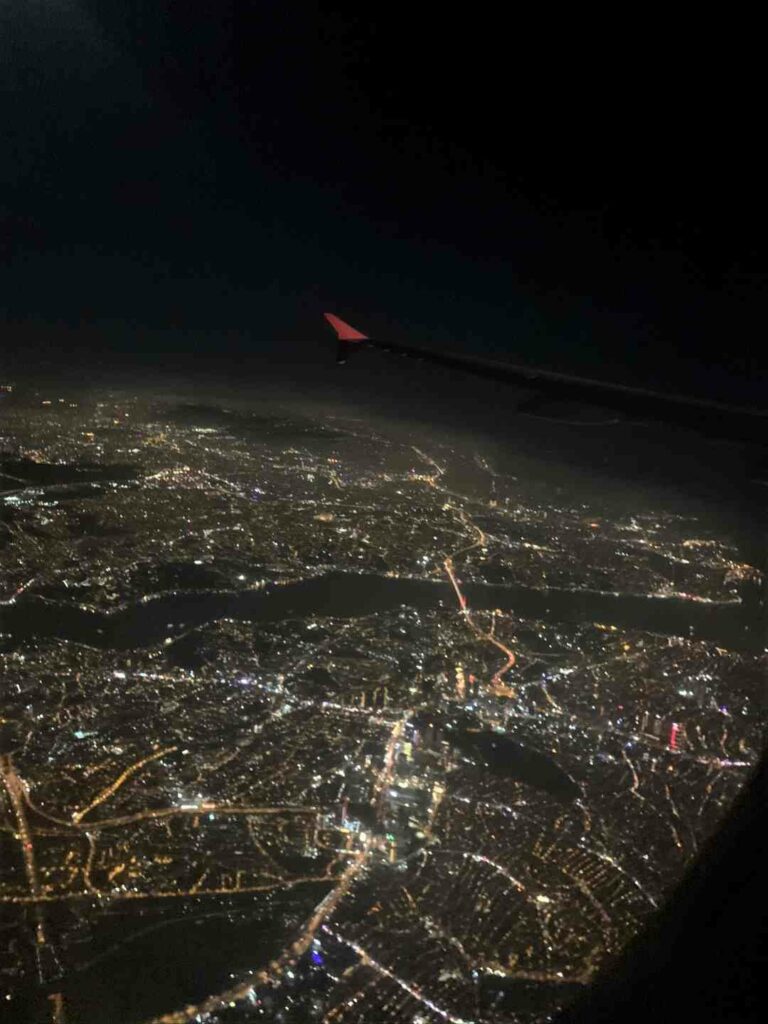 A lit city from a plane at night, towards the black night sky, only the red tip of a wing is visible