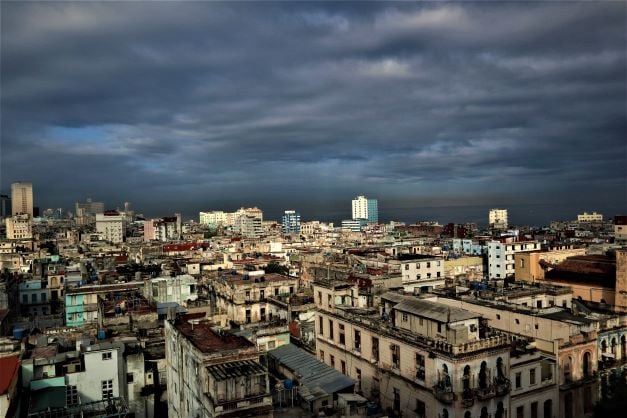The rugged city overview of Central Havana with lots of colonial buildings, against a dark cloudy sky coming in while the sun is still shining on the city