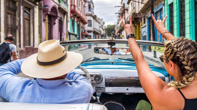 A man and a woman driving a classic American car in Havana Cuba surrounded by colorful classic colonial buildings