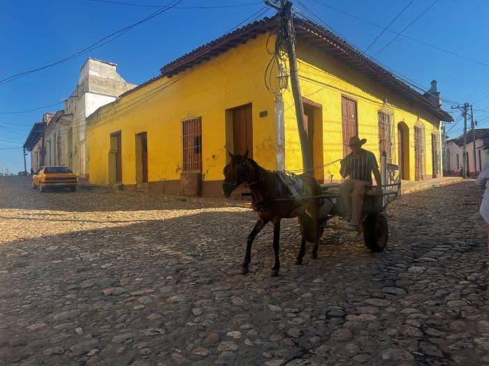 Horse and carriage on cobblestoned street in Trinidad among bright colored houses on a sunny day with blue skies